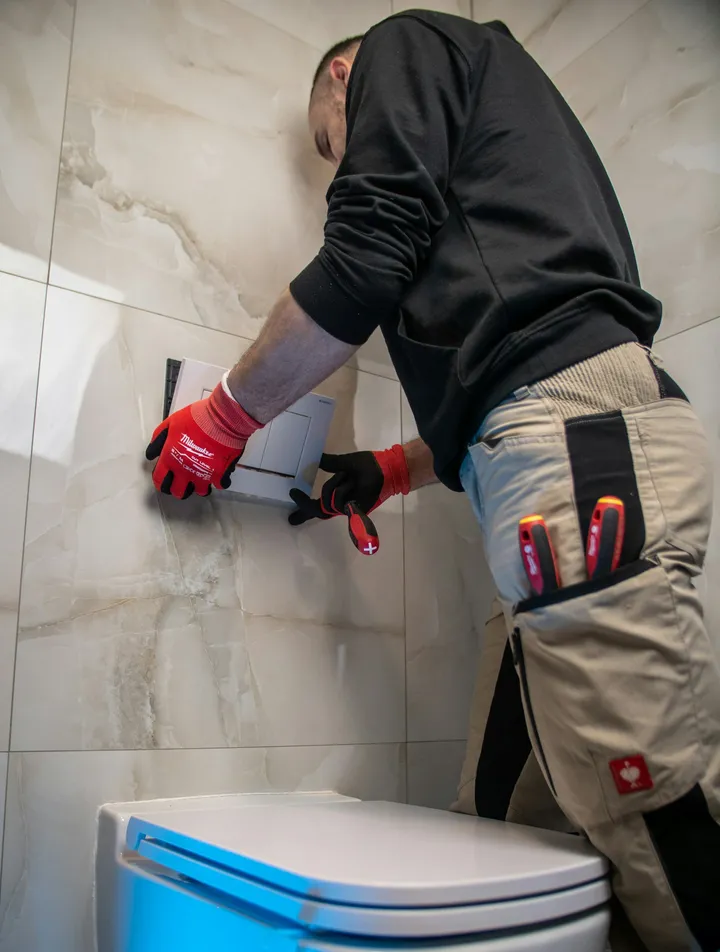 Engineer fitting a flush plate on a tiled bathroom wall